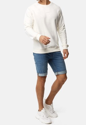 Weißes Sweatshirt mit Rundhalsausschnitt, Jeansshorts mit umgeschlagenen Säumen und weiße Turnschuhe. Lässiges Outfit mit strukturiertem Stoff und lockerem Schnitt.