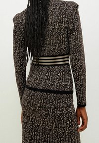Donna con lunghi capelli intrecciati che indossa un vestito con stampa animale nei toni marrone e nero, con una vita a righe, vista da dietro.