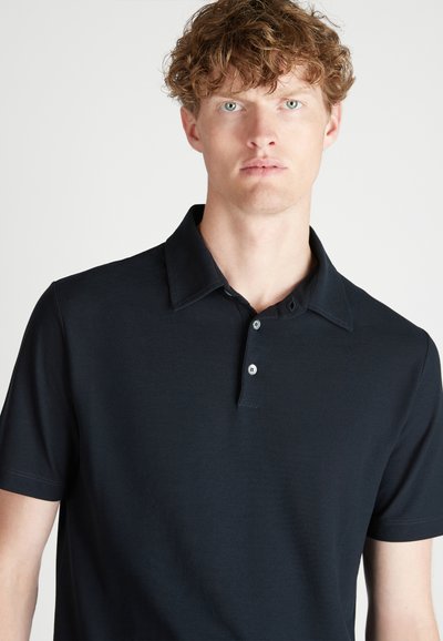 Polo de color azul marino con cuello plano, tapeta de tres botones, mangas cortas y una textura suave. Sin patrones ni acentos visibles.