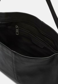 Zwarte lederen handtas interieur met een ritsvak en een soepele textuur. Het ontwerp is minimaal met een zichtbaar gelabeld merketiket.