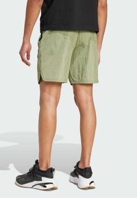 Pantaloni corti verde chiaro con una texture stropicciata, dotati di tasche laterali e orlo dritto. Abbinati a scarpe da ginnastica nere e un top nero.