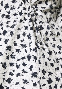 Hvidt stof med et marineblåt blomsterprint, der har et samlet design og snoretrækdetaljer, som skaber tekstur og visuel interesse.