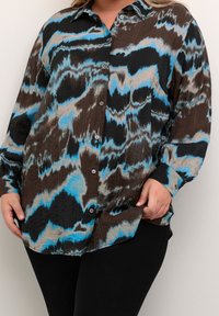 Skjorte med knapper og et flerfarvet abstrakt mønster i brun, sort og blå. Har krave og lange ærmer. Tekstureret stof.