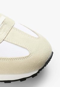 Sneaker mit einem beigen Wildleder-Obermaterial und weißen Mesh-Einsätzen. Runde Zehenpartie und schwarze Gummisohle mit Profil.