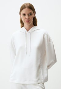 Biała bluza z kapturem o luźnym kroju, wykonana z miękkiej bawełny, z sznurkiem przy szyi i opadającymi ramionami, idealna na swobodny look.