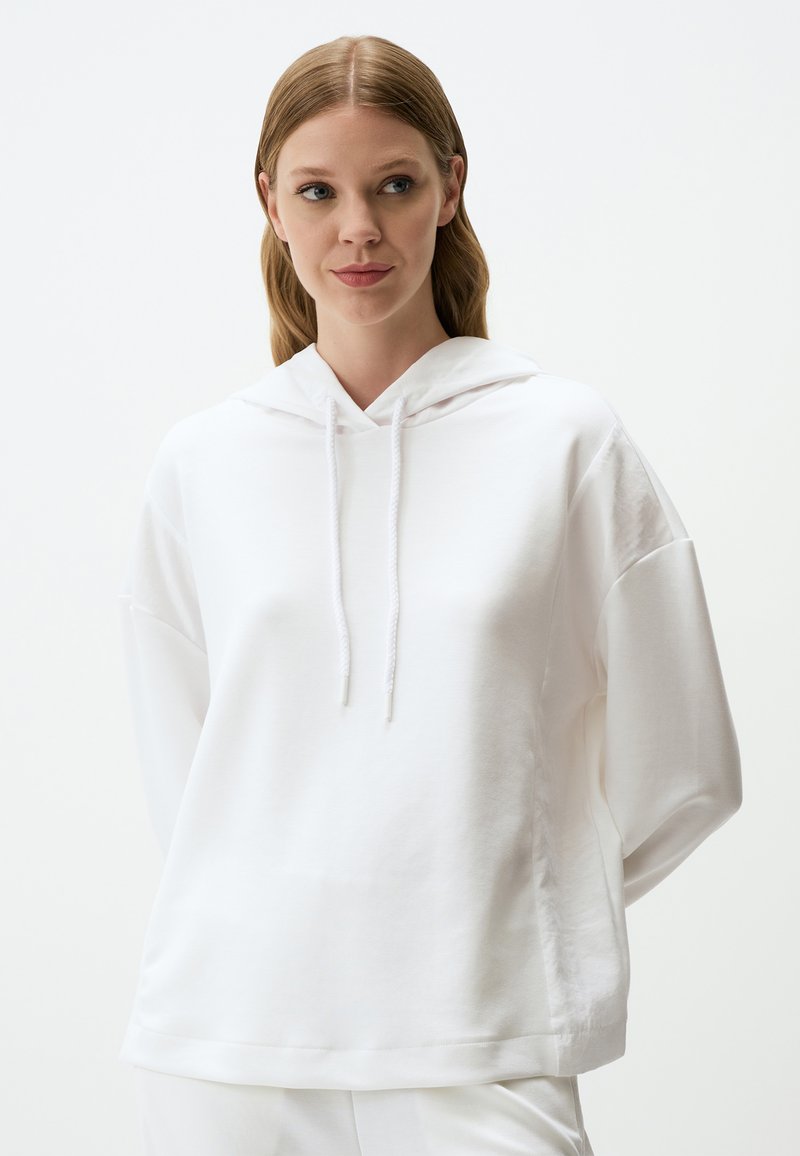 Biała bluza z kapturem o luźnym kroju, wykonana z miękkiej bawełny, z sznurkiem przy szyi i opadającymi ramionami, idealna na swobodny look.