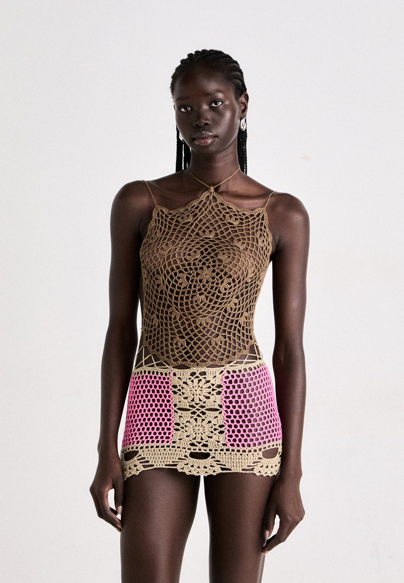 Top in crochet marrone con motivi intricati, abbinato a una mini gonna in crochet rosa e beige con design floreali e dettagli a taglio.