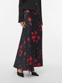 Maxi skirt in dark fabric adorned with red roses, featuring a flowing design and subtle sheen; paired with black pointed heels.