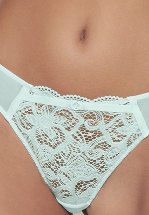 White lace underwear with floral patterns worn on a person’s lower abdomen and hips, showing detailed fabric texture and mesh sides.