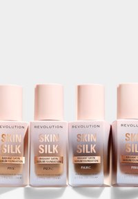 Four bottles of Revolution Skin Silk Radiant Satin Serum Foundation. Each bottle is light pink with gold accents, displaying shade numbers F11.5C, F12.7NC, F14.9C, F15.0N.