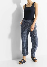 Navy-patterned wide-leg pants with an elastic waistband and side pockets, paired with a fitted black tank top and dark sandals.