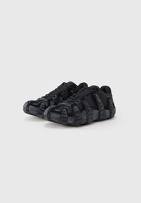 Sorte chunky sneakers med tykke, segmenterede såler og snørebånd, vist side om side på en ensartet lys baggrund.
