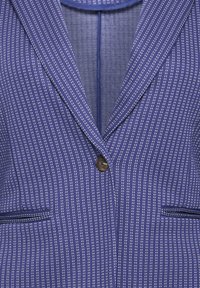 Blazer azul marino con un patrón de rayas, dos bolsillos frontales, solapas con muesca y un cierre de un solo botón marrón. Tela texturizada.