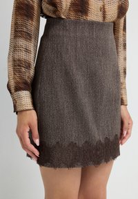 Gonna a scacchi marrone con un tessuto testurizzato, caratterizzata da un orlo a pizzo scallop. Il design aderente mette in risalto la silhouette.