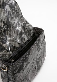 Malá kabelka s otevřeným klopou zobrazující vzor hadí kůže a vnitřní přihrádkou na zip, na bílém pozadí.