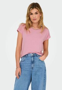 T-shirt rosa a maniche corte con una vestibilità rilassata, abbinata a jeans in denim blu a vita alta, completata da una collana di catena in argento.
