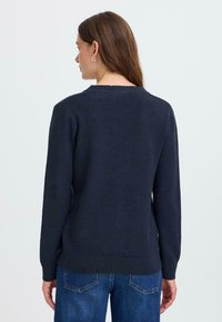 Pull en tricot bleu marine foncé à manches longues et encolure ronde, avec un ourlet et des poignets côtelés, associé à un jean bleu.