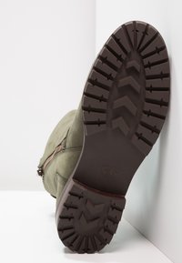 Olivově zelená nubuková bota s texturovanou gumovou podrážkou, která má vzor zigzag, a boční zip pro snadné obouvání.
