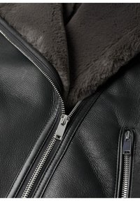Giacca in pelle nera con un colletto in pelliccia sintetica grigia, caratterizzata da cerniere argentate, una superficie testurizzata e cuciture a vista lungo i bordi.
