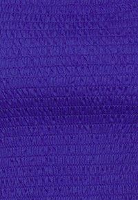 Lila texturerad tyg med ribbdesign som har växelvis upphöjda och plana områden, vilket skapar ett visuellt dynamiskt mönster.