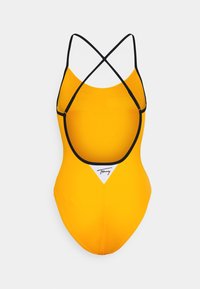Costume da bagno intero giallo con schiena bassa, spalline incrociate e dettagli neri. Include un logo triangolare sul davanti. Texture liscia.