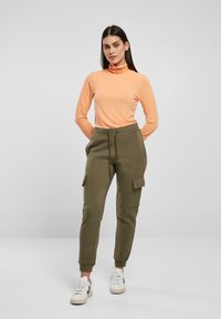 Maglione a collo alto arancione a maniche lunghe abbinato a jogger cargo verde oliva con tasche laterali e polsini a coste, completato da sneaker bianche.