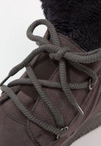 Stivale grigio in suede con rivestimento in finta pelliccia nera, presenta lacci grigi rotondi intrecciati attraverso occhielli in metallo e una suola in gomma testurizzata.