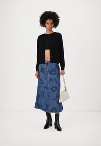 Svart cardigan med knappeåpning, blå denimskjørt med stort blomstermønster, svarte hælboots og en beige crossover-veske.