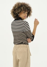 Svart och beige randig stickad tröja med hög krage, trekvartsärmar, ihop med beige byxor med elastisk midja.