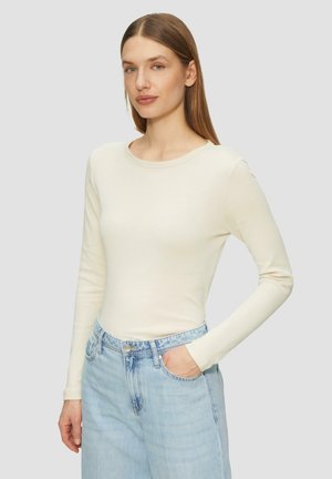 Langärmliges, cremefarbenes Oberteil aus weichem Stoff mit Rundhalsausschnitt, kombiniert mit hellblauen Jeans und einem schlichten Taschen Design.