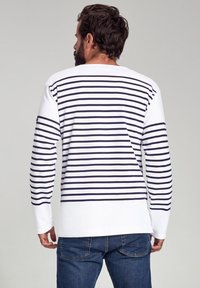 Langærmet hvid skjorte med marineblå horisontale striber, med rund halsudskæring og afslappet pasform. Bæres med blå denimjeans.