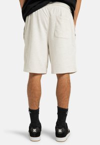 Light gray cotton shorts with an elastic waistband, side pockets, and a back pocket. Pair of black shoes with white accents and black socks.