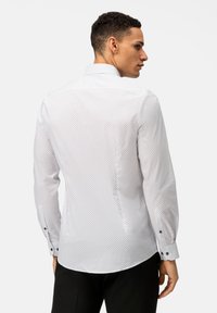 Chemise blanche à motif à pois, à manches longues, avec un col pointu et des poignets à boutons. Tissu lisse avec une coupe ajustée.