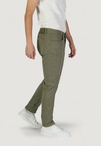 Pantalones ajustados de color verde oliva con diseño de múltiples bolsillos, material de algodón, costuras visibles y combinados con zapatillas blancas.