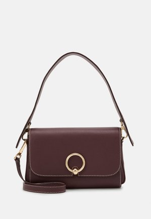 Sac à main en cuir marron foncé avec fermoir circulaire doré, doubles sangles amovibles et coutures blanches sur fond uni.