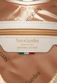 Étiquette intérieure en cuir véritable crème et or, portant les inscriptions "NeroGiardini", "Fabriqué en Italie" et un petit drapeau italien ; texture satinée.