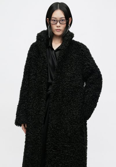 Casaco de pêlo sintético preto com uma superfície texturizada e encaracolada, frente aberta e grande gola. O design apresenta mangas longas e um corte descontraído.