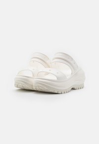 Zuecos blancos con un diseño abierto, que presentan dobles correas, agujeros de ventilación circulares y una suela gruesa y texturizada para mayor agarre.