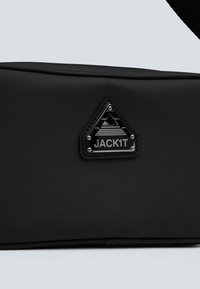 Sort crossbody taske lavet af glat materiale, med en trekantet lap med præget tekst "JACK1T" og geometrisk design.