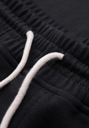 Nærbillede af sort sweatpants taljebånd med hvid snøre trækket gennem ribbet elastisk bånd.