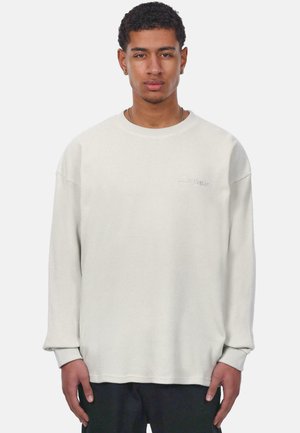 Waffle-knit long-sleeve sweatshirt in light beige, featuring a crew neck and ribbed cuffs. Subtle logo embroidery on chest.