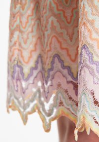 Ourlet d'une robe en dentelle mettant en avant des motifs en vagues dans des couleurs pastel—pêche, lavande, menthe—brodés avec des fils métalliques pour un léger éclat et une texture.