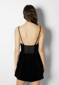 Svart sammet mini klänning med tunna justerbara band, plisserad byst och en genomskinlig panel baktill med en dold dragkedja.