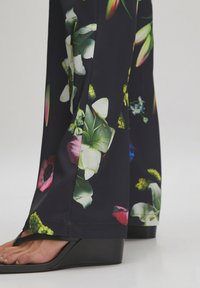 Zwart stoffen wijde broek met een bloemenprint. Bevat levendige bloemen in tinten roze, groen en blauw. Inclusief een splitdetail.