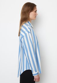 Camicia a strisce blu chiaro e bianca con una vestibilità rilassata, maniche lunghe e orlo curvo. Realizzata in un tessuto morbido con bottoni sui polsini.