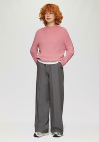 Lichtroze, geribbelde gebreide trui met ronde hals, gecombineerd met hoge, wijde grijze broeken en zilveren sneakers.