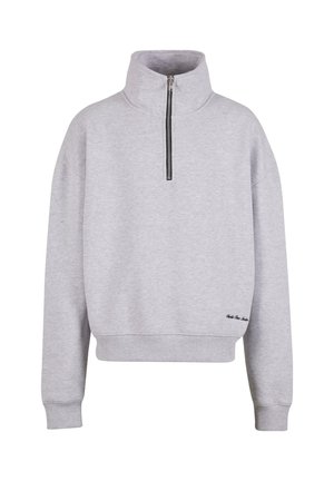Sweatshirt gris clair avec un col montant, fermeture à zip quart, et poignets côtelés. Présente un petit accent noir brodé près de l'ourlet.