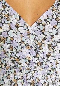 Robe portefeuille fleurie avec un décolleté en V, une taille froncée, et un fond noir orné de fleurs pastel aux teintes lavande, vert et marron.