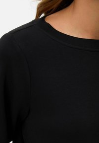 Sudadera negra con una textura suave, escote redondeado y costuras visibles en los hombros. Diseño simple y clásico.