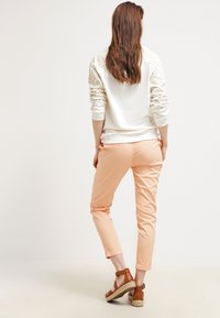 Biała bluza z teksturowanymi, prążkowanymi rękawami, zestawiona z jasnoróżowymi, dopasowanymi spodniami oraz brązowymi sandałami na kostkę z espadrille'owymi podeszwami.